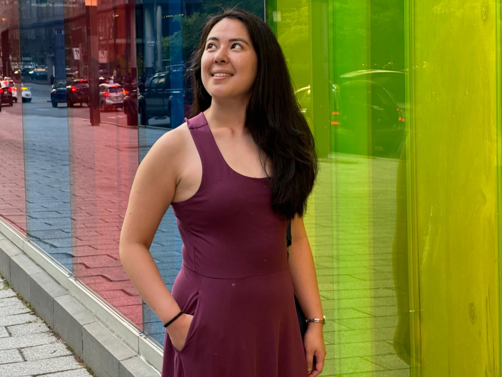 Woman standing in front of colourful windows wearing a red dress. 