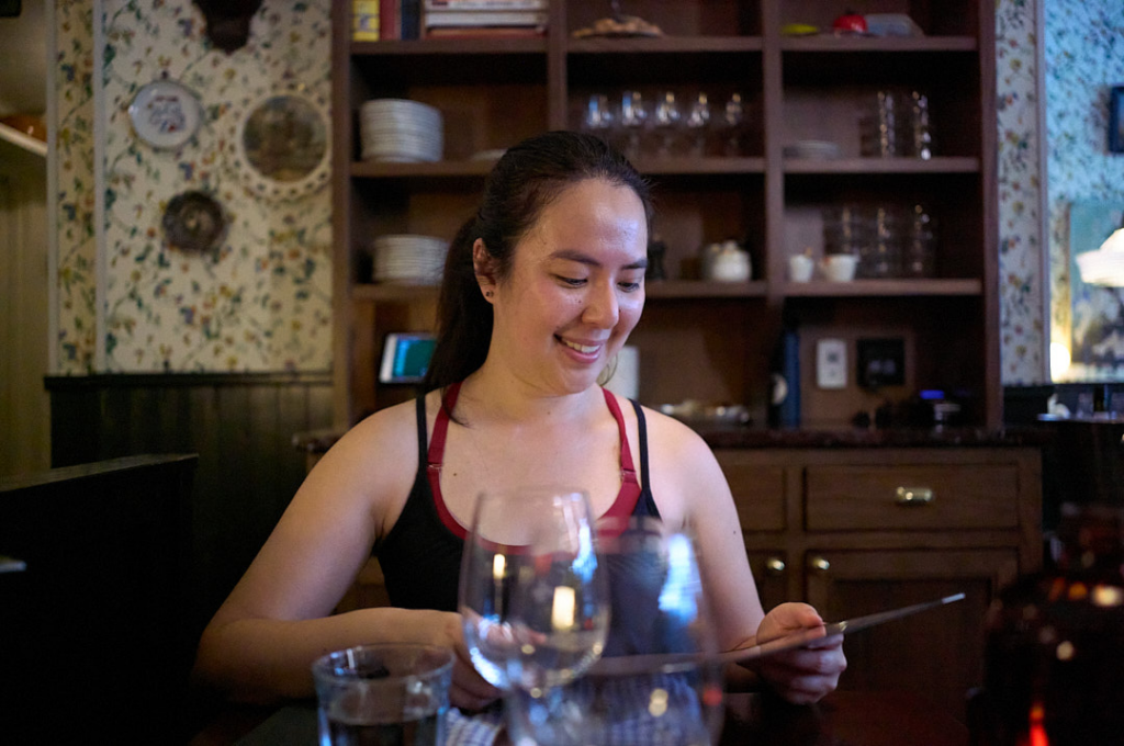 Woman smiling while holding a menu and surrounded by wine glasses. 