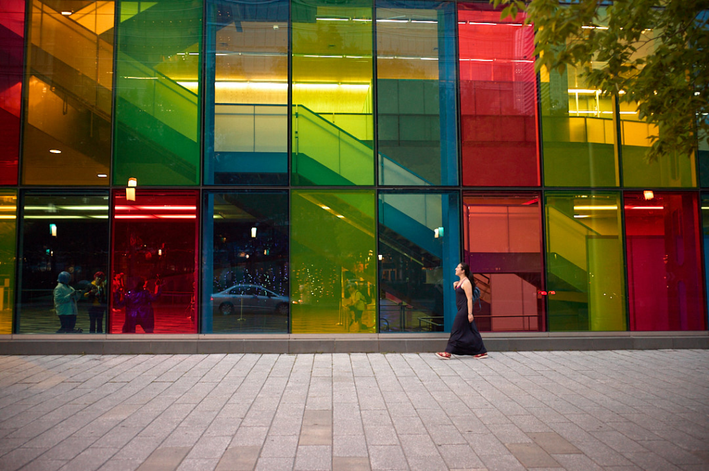 Woman walking across the street with colourful windows in the background. 