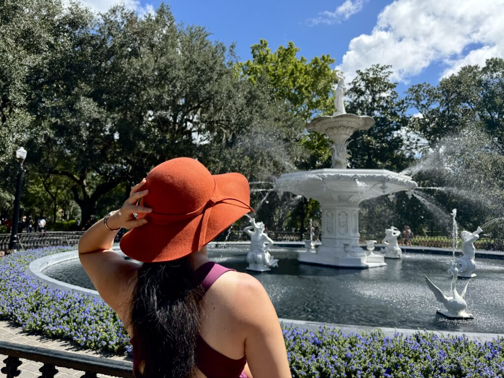 Woman wearing large hat and standing in front of fountain in Forsyth Park Savannah. 