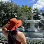 Woman wearing large hat and standing in front of fountain in Forsyth Park Savannah.