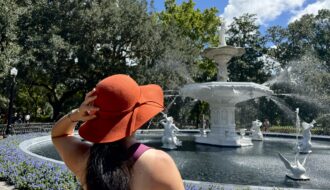 Woman wearing large hat and standing in front of fountain in Forsyth Park Savannah.