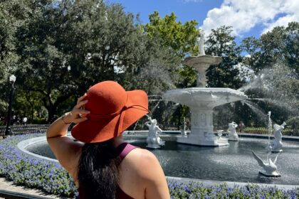 Woman wearing large hat and standing in front of fountain in Forsyth Park Savannah.