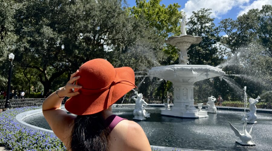 Woman wearing large hat and standing in front of fountain in Forsyth Park Savannah.