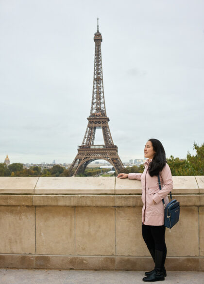 woman standing in front of a ledge facing the eiffel tower in paris, france