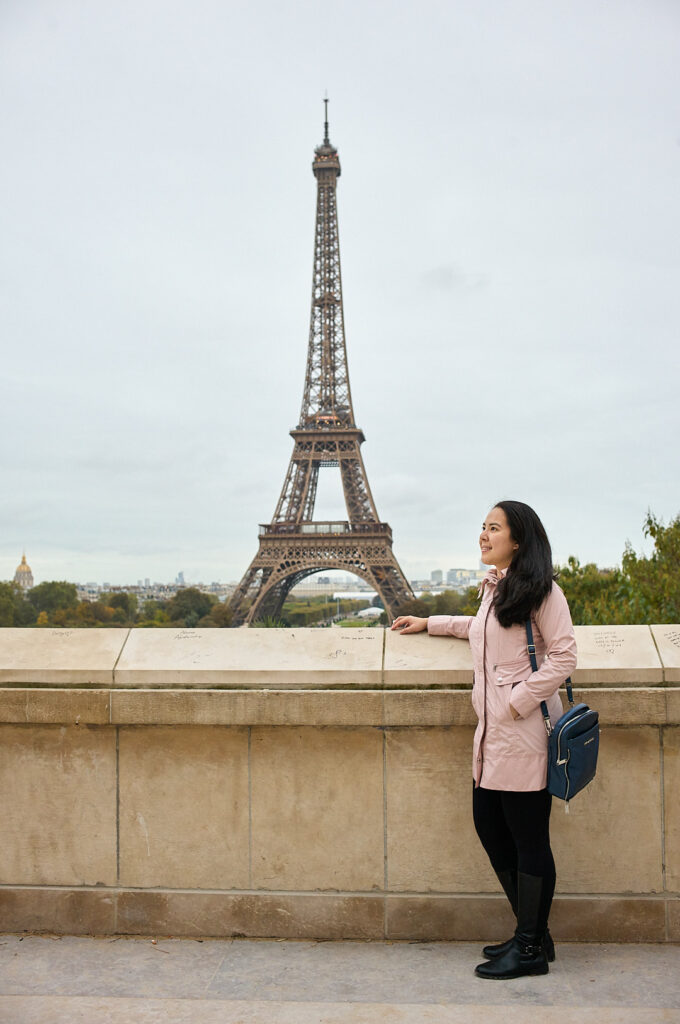 woman standing in front of a ledge facing the eiffel tower in paris, france