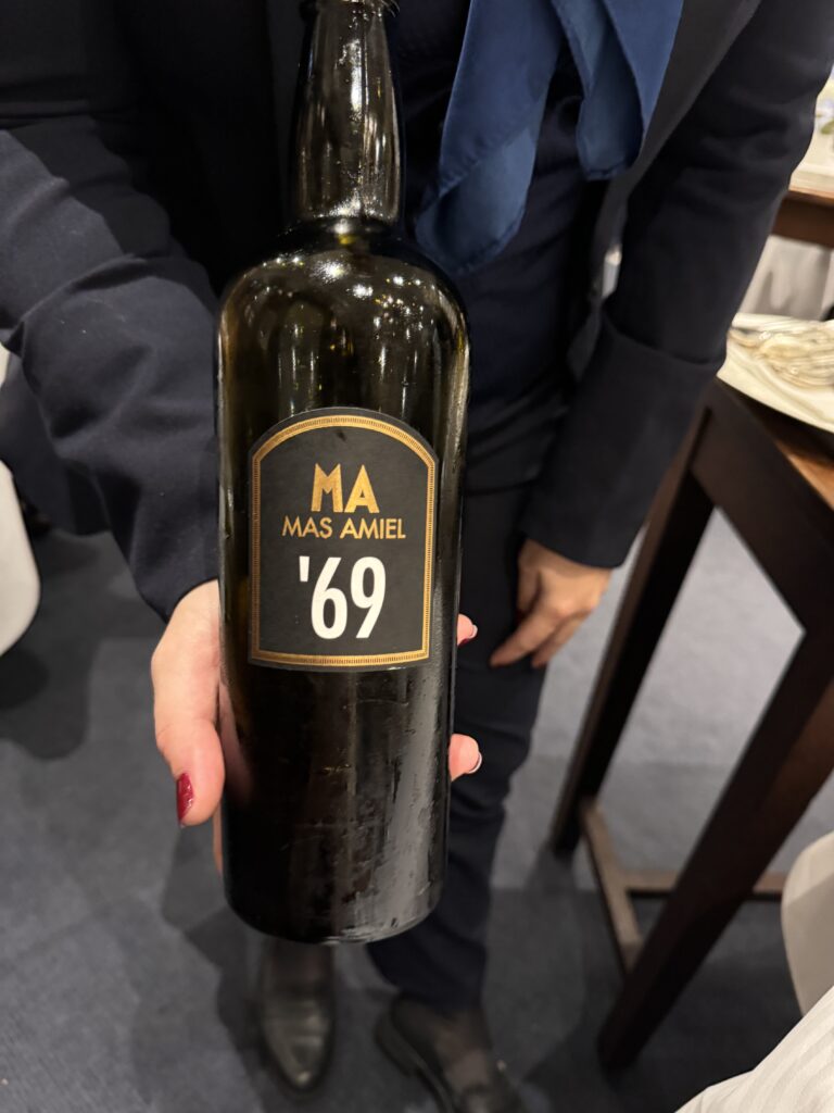 Person holding a bottle of port wine with the label 1969 and Mas Amiel on it. 