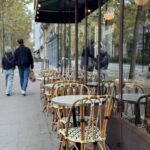 A man and woman walking past bar chairs in paris.