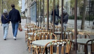 A man and woman walking past bar chairs in paris.