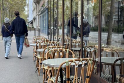 A man and woman walking past bar chairs in paris.