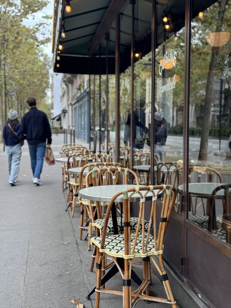 A man and woman walking past bar chairs in paris. 