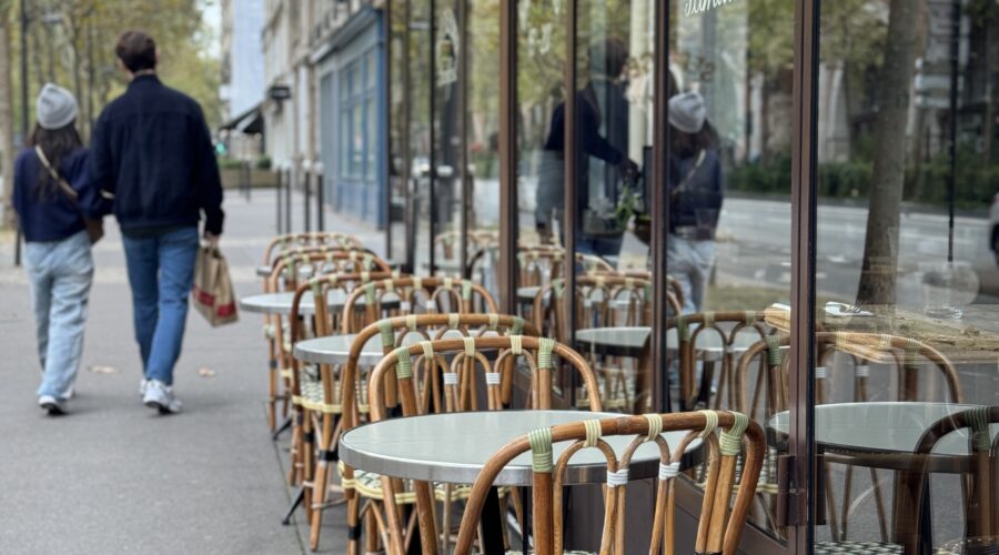 A man and woman walking past bar chairs in paris.