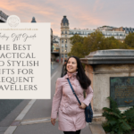 A woman wearing a vibrant pink coat and carrying a stylish blue bag strolls along a cobblestone street in Paris. The scene features iconic Parisian architecture in the background, with ornate balconies and decorative ironwork. She appears to be enjoying the crisp weather, her hair slightly tousled by the breeze, as she walks past charming cafes and boutique storefronts.